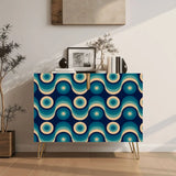 Retro wooden cabinet with blue and teal retro circle doors and hairpin legs with a tall plant and framed art in a bright room