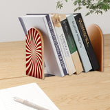 Red Sunburst retro bookend holding books on a wooden desk next to a pen