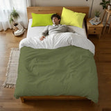 Person lying on a bed under the olive green duvet cover with lime pillowcases, seen from above