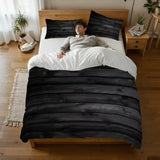 Person lying on a bed under the black wood plank duvet cover, seen from above