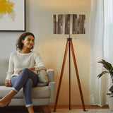 Gray Barnwood Print retro tripod floor lamp with wooden legs and remote, cozy living room, woman relaxing on a sofa