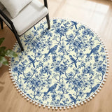 Cream round rug with blue toile floral and bird print and white pom pom edge beside an armchair