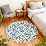 Blue toile round rug with pom poms beside a bed and small wooden side table