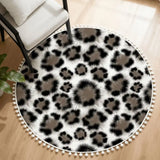 Gray and black leopard print round rug with white pom pom edge beside a white armchair