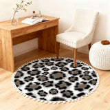 Gray leopard print round rug with pom poms in front of a wooden desk and white chair