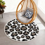 Gray leopard print round rug with pom poms under a hanging rattan egg chair