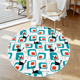 Round rug with white border, teal squares and black cats beside a white armchair on a wood floor